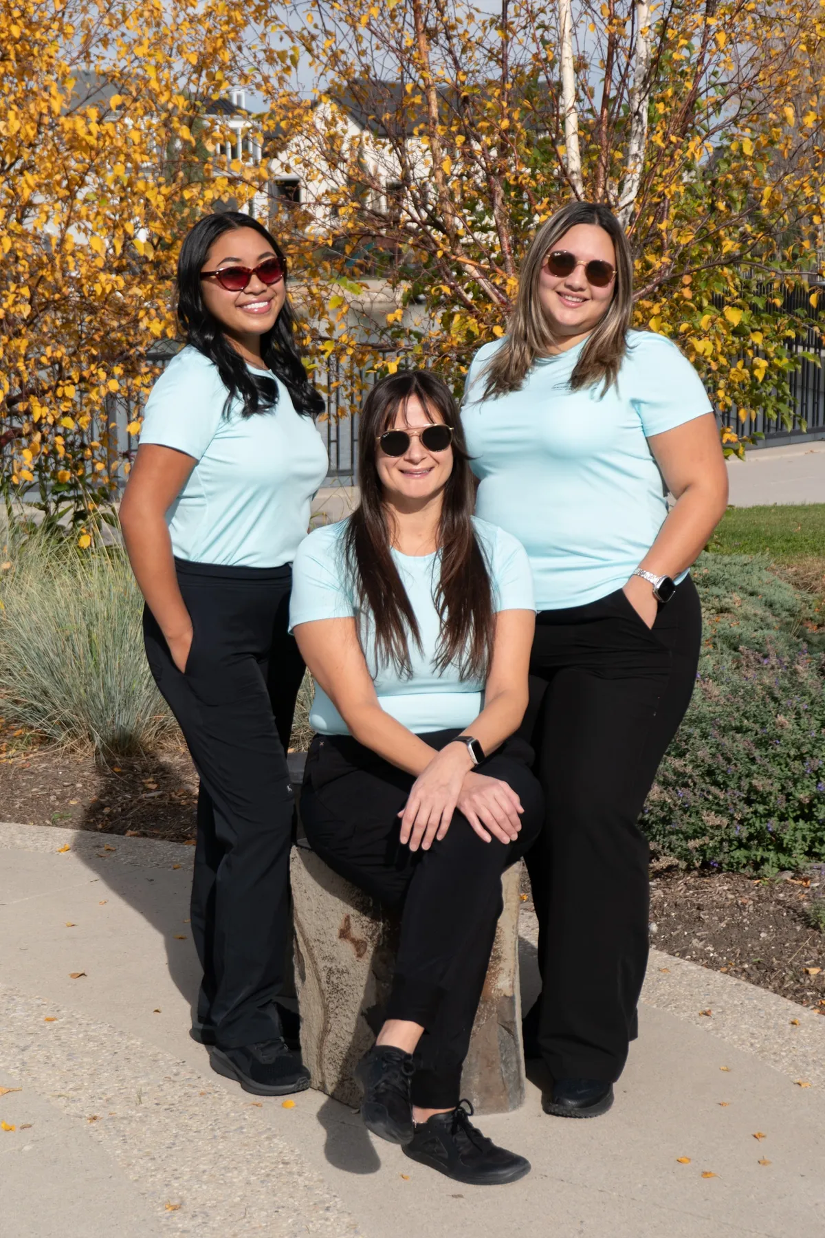 Three Mahogany Village Dental team members in sunglasses posing together outdoors among yellow autumn trees