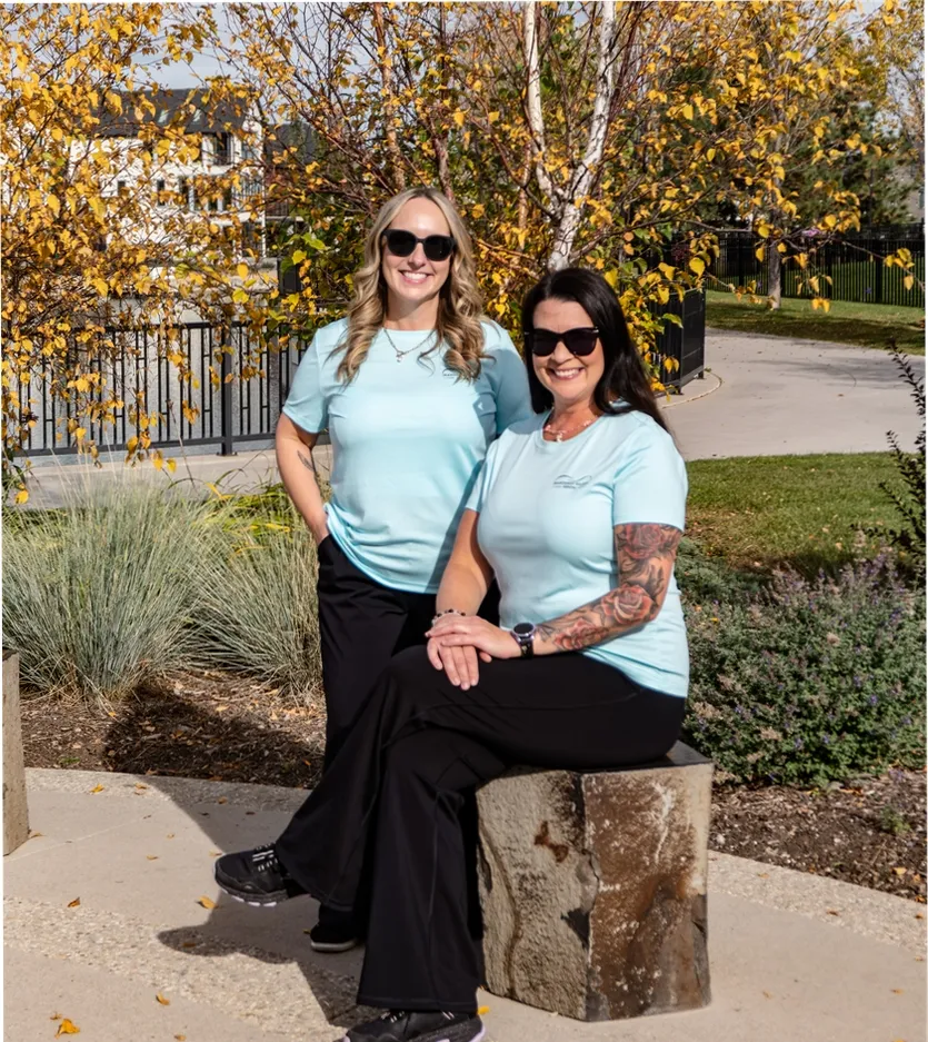 Two Mahogany Village Dental team members in sunglasses posing outdoors among yellow autumn trees